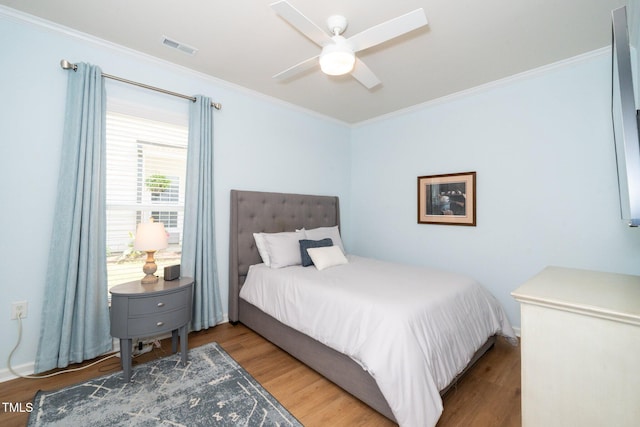 bedroom with visible vents, crown molding, wood finished floors, and ceiling fan
