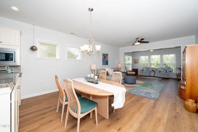 dining area featuring visible vents, light wood-type flooring, baseboards, ceiling fan with notable chandelier, and ornamental molding