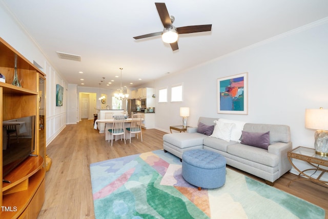 living room with visible vents, baseboards, ceiling fan with notable chandelier, ornamental molding, and light wood-style flooring