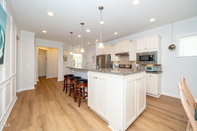 kitchen featuring light wood-style floors, decorative backsplash, under cabinet range hood, and stainless steel appliances
