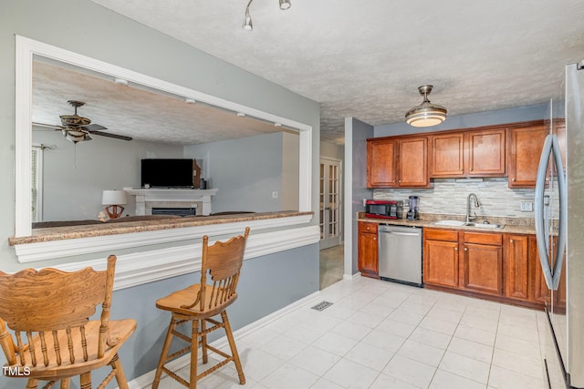 8404 Frenchorn Ln, Fayetteville, NC 28314 - kitchen with brown cabinetry, a sink, stainless steel appliances, a textured ceiling, and backsplash