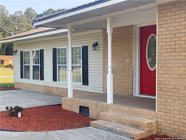 view of exterior entry featuring covered porch and brick siding