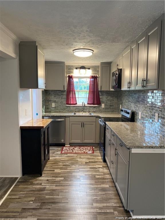 kitchen featuring tasteful backsplash, dark wood-type flooring, gray cabinets, stainless steel appliances, and a sink
