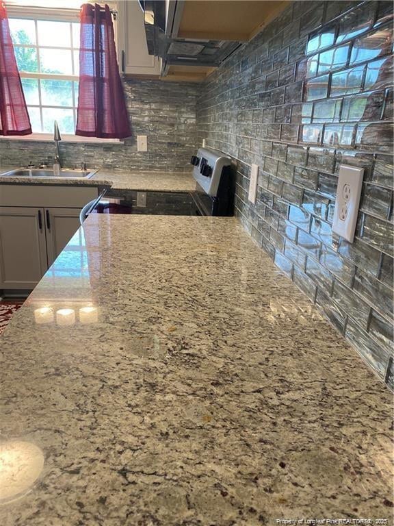 kitchen with stove, tasteful backsplash, light stone counters, and a sink