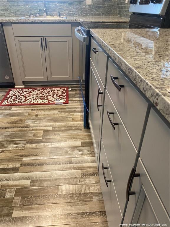 kitchen featuring light stone counters, wood finished floors, gray cabinetry, a sink, and dishwasher