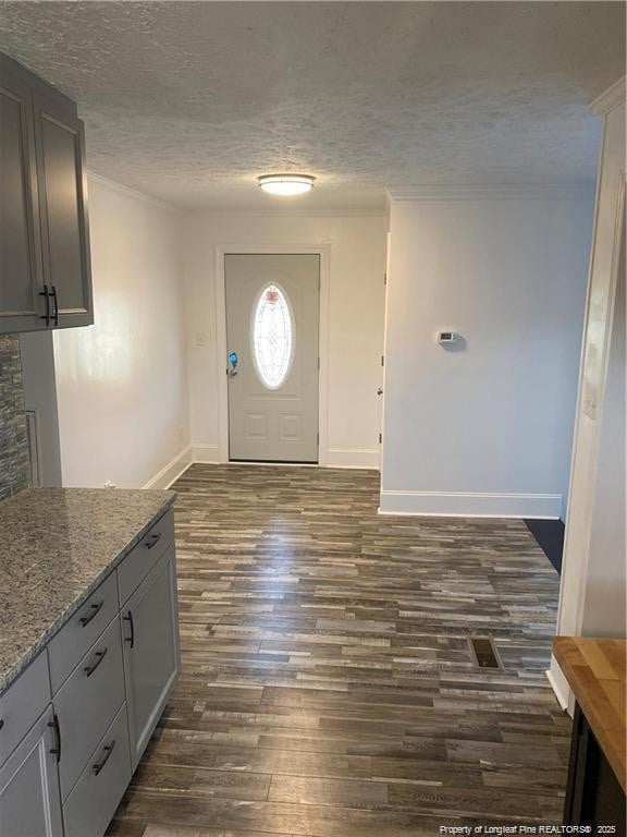 entrance foyer with a textured ceiling, dark wood-style floors, baseboards, and ornamental molding