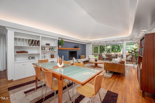 dining area featuring a raised ceiling, a fireplace, and light wood finished floors