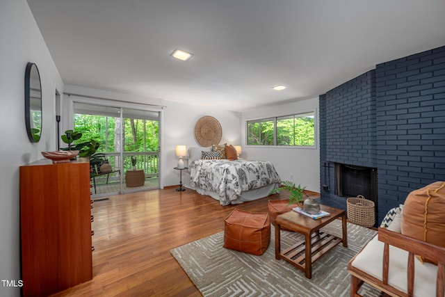bedroom featuring a brick fireplace, access to outside, and wood finished floors