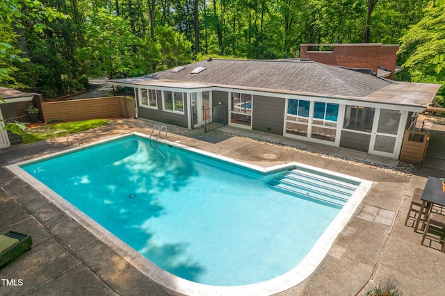 view of swimming pool featuring fence, a sunroom, a fenced in pool, a patio area, and a forest view