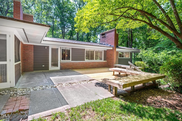 rear view of house with brick siding, a chimney, a patio area, and a wooden deck