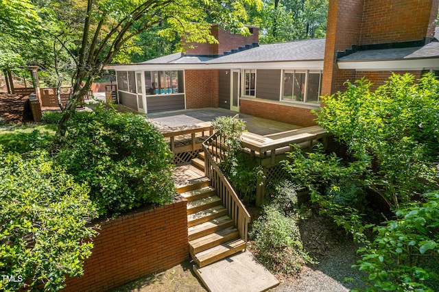 exterior space featuring a shingled roof, brick siding, a sunroom, a deck, and a chimney