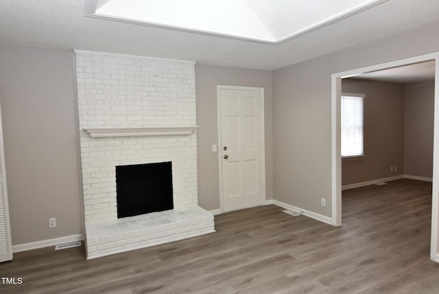 107 Ware Ct, Garner, NC 27529 - unfurnished living room featuring baseboards, a textured ceiling, visible vents, a brick fireplace, and wood finished floors
