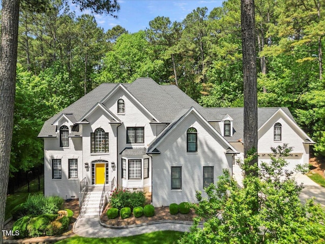 1508 Tradescant Ct, Raleigh, NC 27613 - french provincial home with concrete driveway, view of wooded area, a garage, and roof with shingles