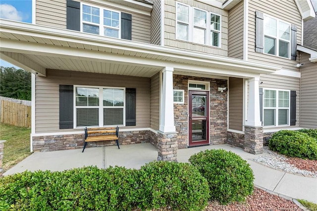 doorway to property with stone siding, covered porch, and fence