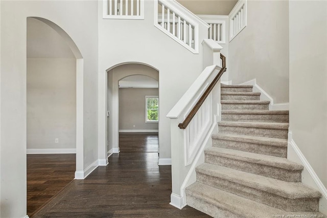 staircase featuring arched walkways, wood finished floors, and baseboards