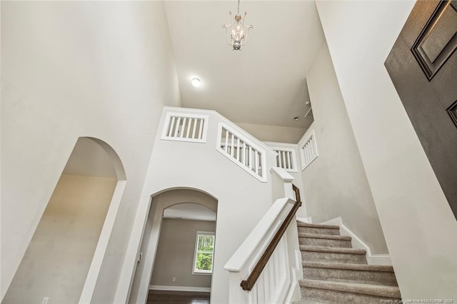 staircase with a towering ceiling, arched walkways, a chandelier, and baseboards