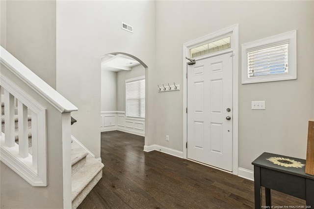 foyer entrance with arched walkways, wood finished floors, stairs, and a wainscoted wall