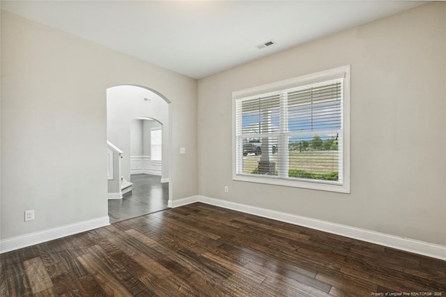 spare room with arched walkways, dark wood-style flooring, baseboards, and stairway