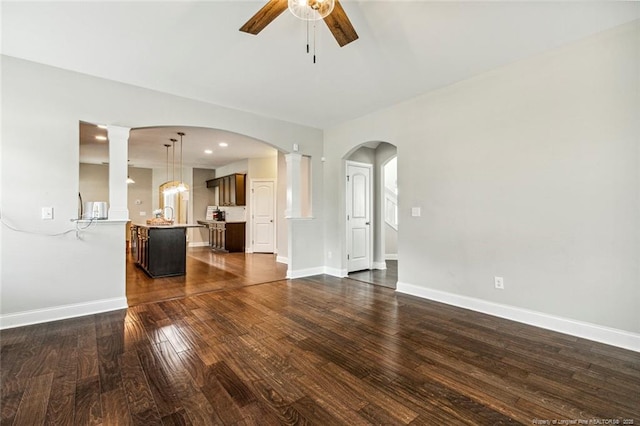 unfurnished living room featuring a ceiling fan, dark wood-style floors, baseboards, and decorative columns