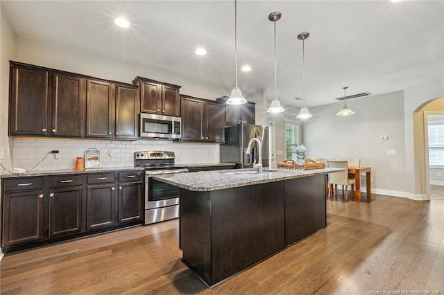 kitchen featuring stainless steel appliances, arched walkways, backsplash, light stone countertops, and recessed lighting