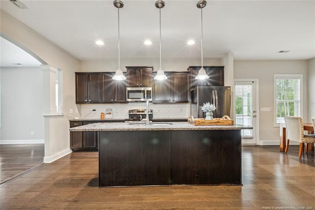 kitchen with appliances with stainless steel finishes, a sink, a center island with sink, dark brown cabinetry, and baseboards