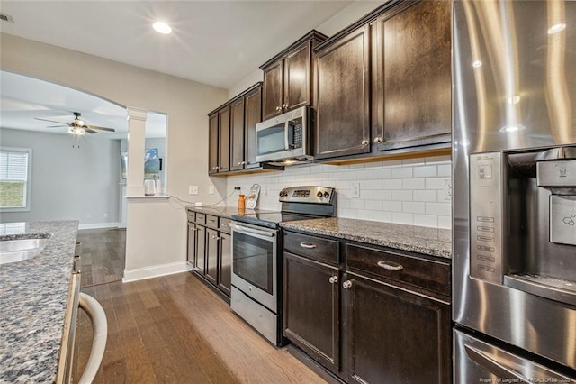 kitchen featuring appliances with stainless steel finishes, ornate columns, dark wood-style floors, dark brown cabinets, and stone counters