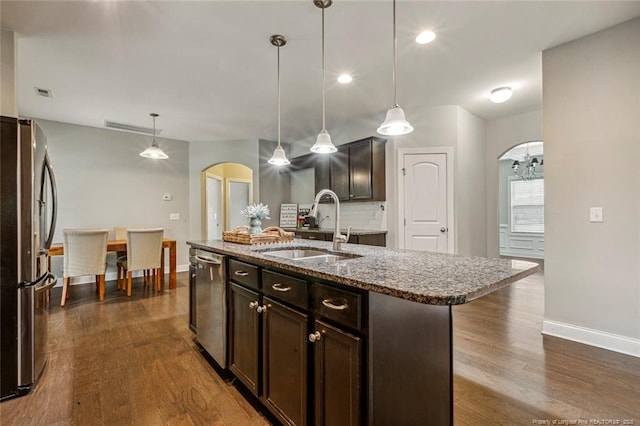 kitchen with stainless steel appliances, a sink, arched walkways, baseboards, and dark wood-style floors