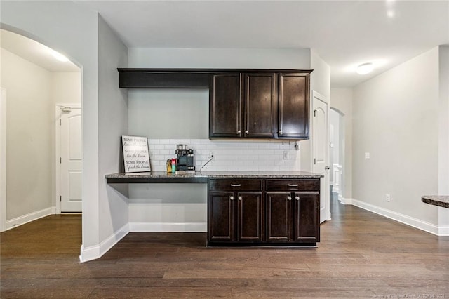 bar area with arched walkways, dark wood finished floors, and decorative backsplash