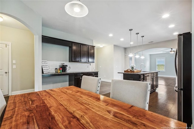 kitchen featuring freestanding refrigerator, arched walkways, dark wood finished floors, a center island with sink, and recessed lighting