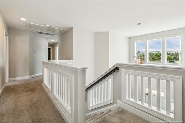 corridor featuring attic access, light colored carpet, and baseboards