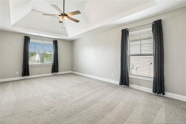 carpeted empty room with a tray ceiling, ceiling fan, and baseboards