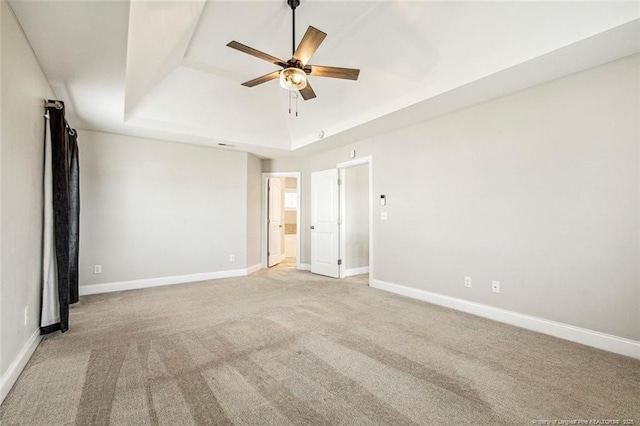 spare room with a raised ceiling, a ceiling fan, light colored carpet, and baseboards