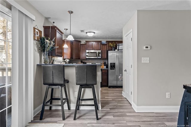 263 Autumn Ln, Raeford, NC 28376 - kitchen with stainless steel appliances, a peninsula, light wood finished floors, hanging light fixtures, and a kitchen bar