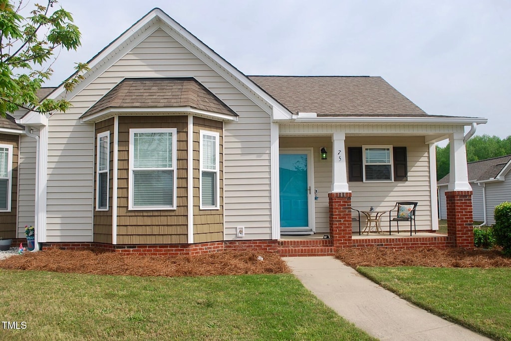 view of front of house featuring a front yard, covered porch, and roof with shingles