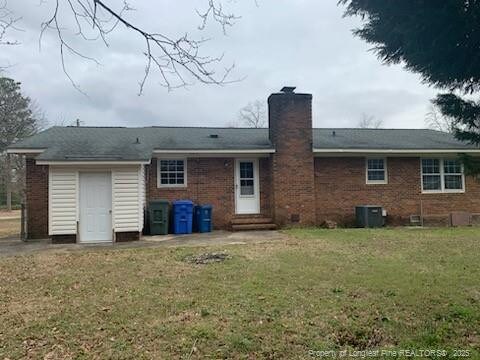 back of property featuring central AC unit, entry steps, a chimney, and a yard