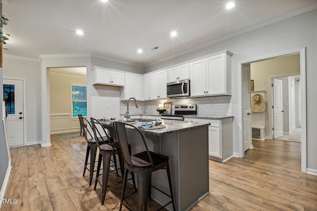 kitchen with appliances with stainless steel finishes, a sink, backsplash, white cabinets, and ornamental molding