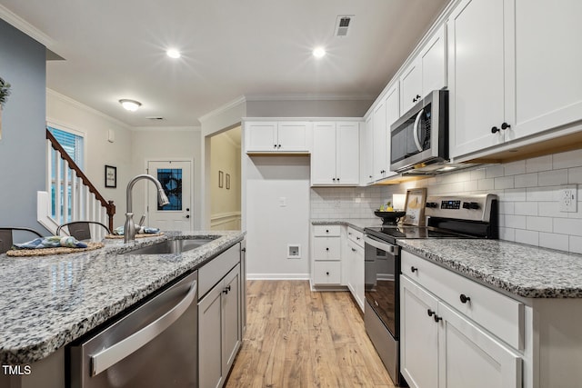 kitchen with stainless steel appliances, a sink, light wood-style flooring, ornamental molding, and light stone counters