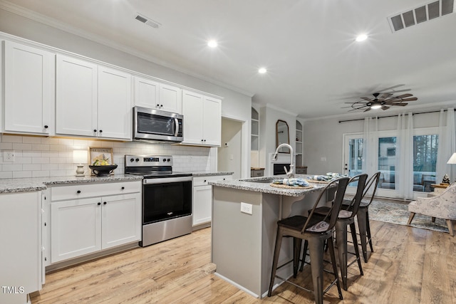 kitchen with stainless steel appliances, a sink, ornamental molding, light wood-style flooring, and white cabinetry