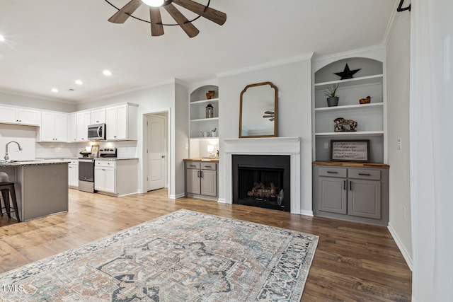 living area featuring a ceiling fan, light wood finished floors, a fireplace, crown molding, and recessed lighting