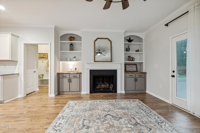 living area with a ceiling fan, a fireplace, ornamental molding, light wood-style flooring, and built in features