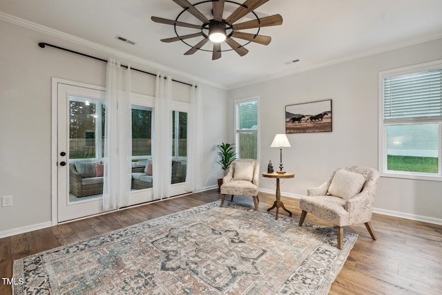 living area with ornamental molding, ceiling fan, wood finished floors, and baseboards