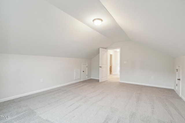 additional living space with vaulted ceiling, light colored carpet, and baseboards
