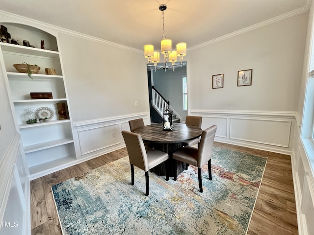 dining space with a chandelier, wood finished floors, crown molding, a wainscoted wall, and a decorative wall