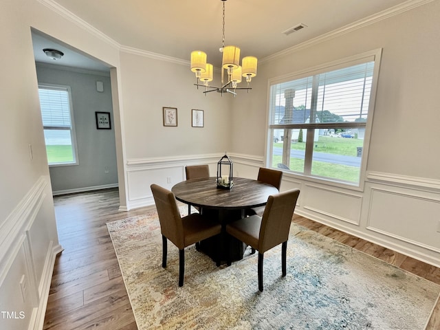 dining room with ornamental molding, a chandelier, wood finished floors, and a wainscoted wall