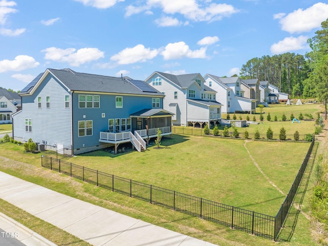 rear view of house with a sunroom, a residential view, a lawn, and a fenced backyard