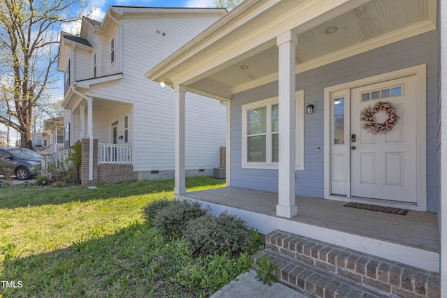 doorway to property featuring crawl space, a lawn, and covered porch