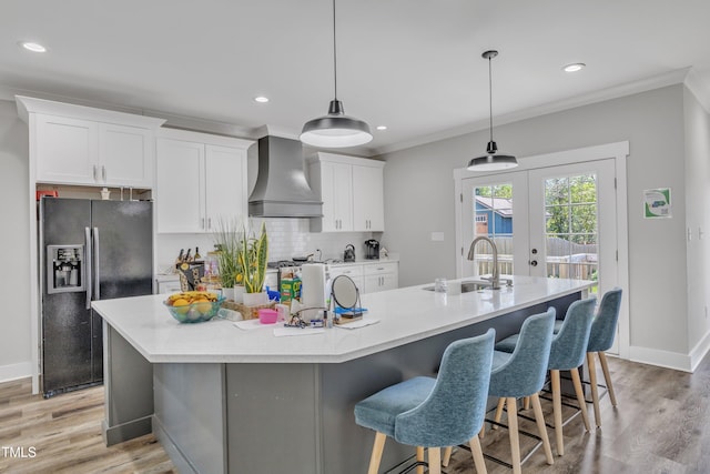 kitchen featuring wall chimney exhaust hood, a large island with sink, white cabinets, black fridge, and a sink