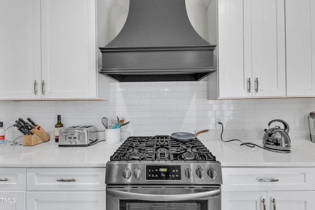 kitchen featuring custom range hood, stainless steel gas range, white cabinets, and backsplash