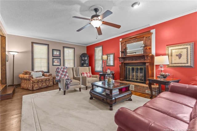 living area featuring a glass covered fireplace, ornamental molding, a textured ceiling, a ceiling fan, and wood finished floors