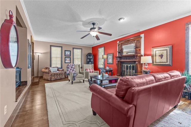 living area featuring a textured ceiling, ornamental molding, ceiling fan, and a glass covered fireplace